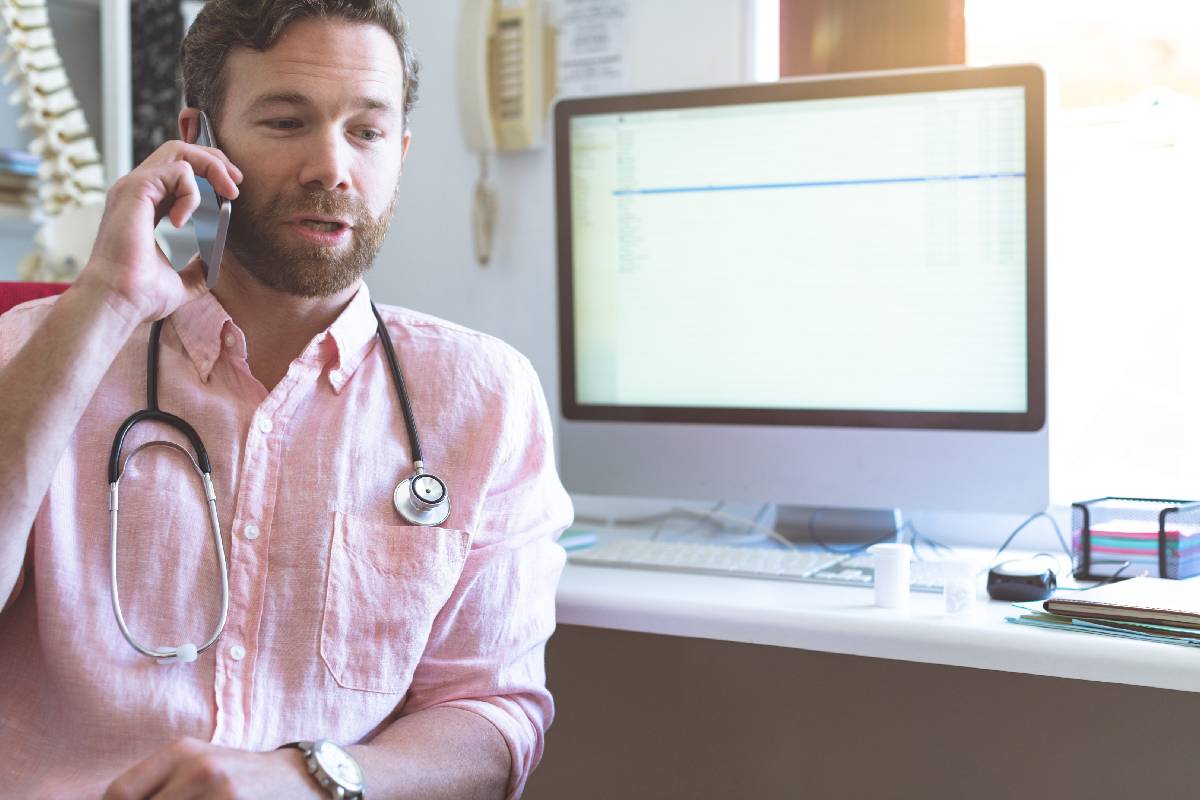 Front view of a Caucasian male doctor talking on mobile phone in clinic against computer in background